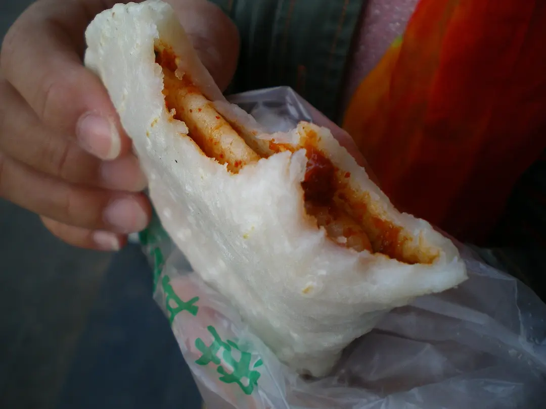 A hand holding a folded grilled rice cake spread with red chili sauce