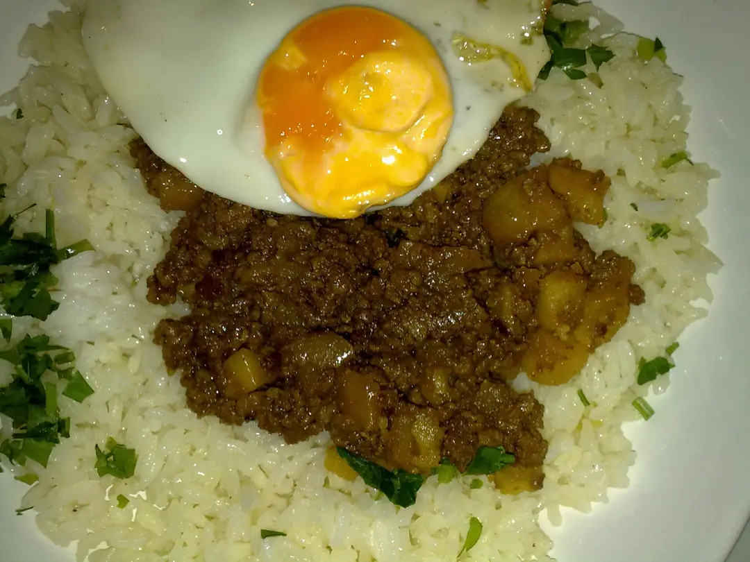 Minced meat with diced potato on white rice, topped with a fried egg