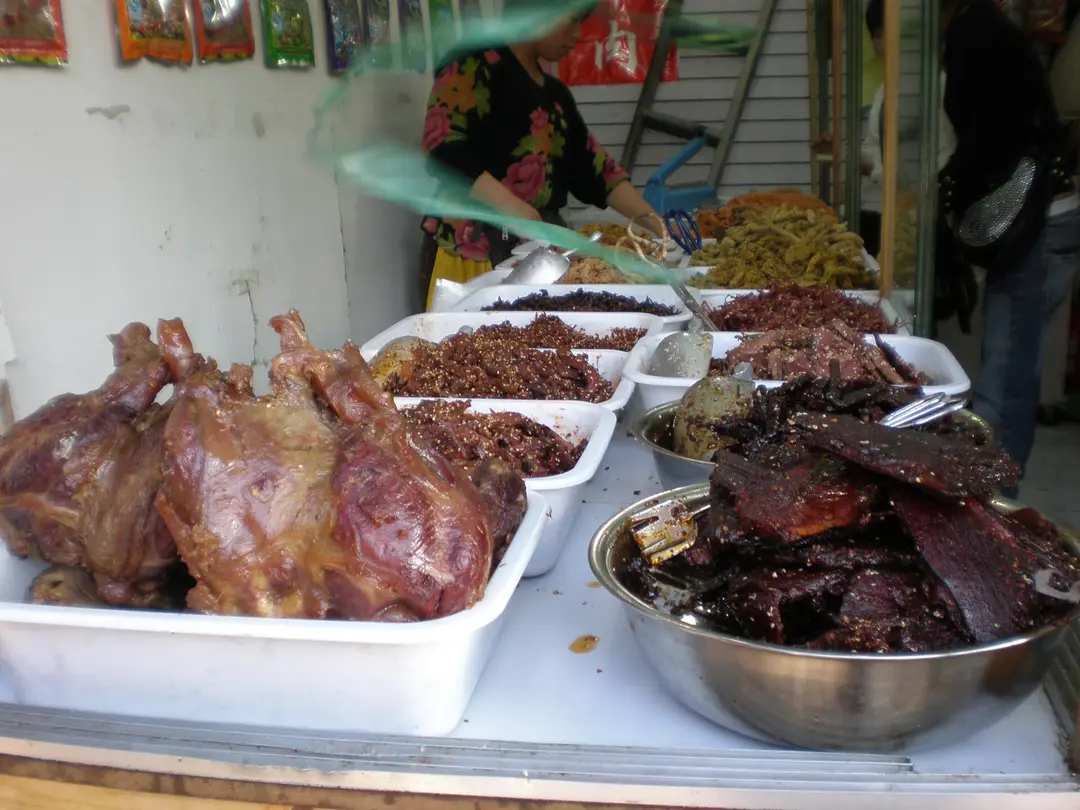 A steel bowl piled with dark dried yak meat and trays of shredded meat on a shop counter