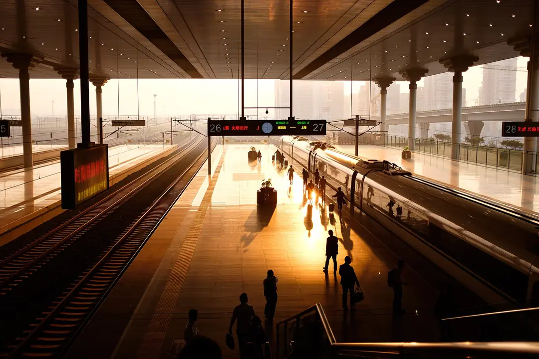Passengers walking along a platform beside a high-speed train at Nanjing South station in early morning light