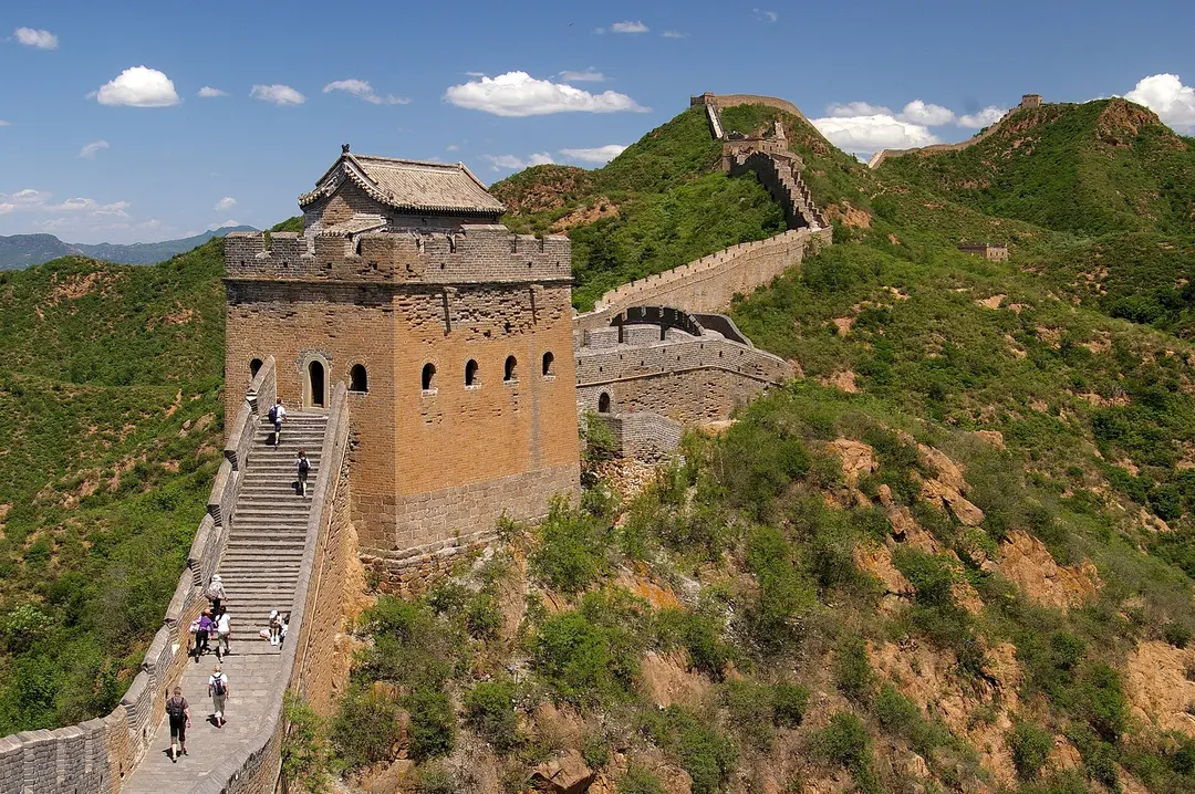 Walkers climbing a watchtower on the Great Wall as it runs over green hills