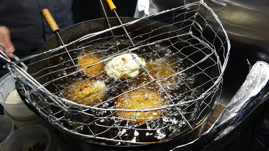 Fuzhou-style oyster cakes frying golden in hot oil inside a wire basket