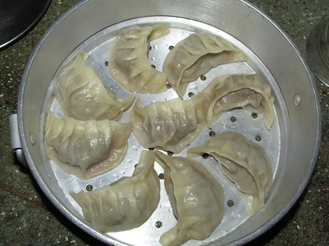 Pleated half-moon dumplings in a round metal steamer tray