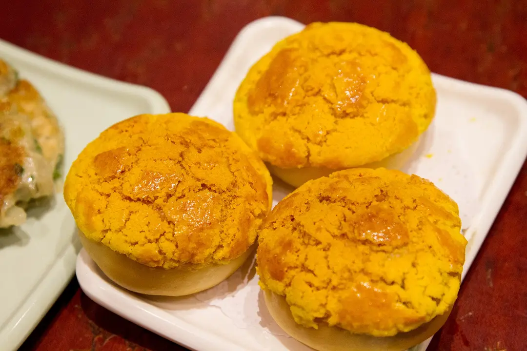 Three pineapple buns with cracked golden tops on a white plate