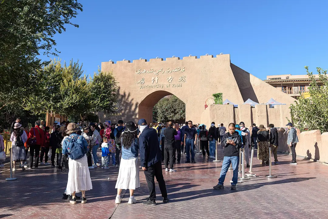 The earth-colored east gate of Kashgar's old town, signed Ancient City of Kashi, with visitors on the plaza in front