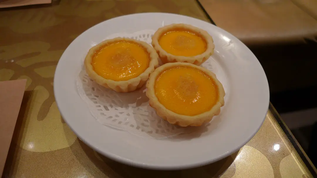 Three egg tarts with yellow custard on a white plate