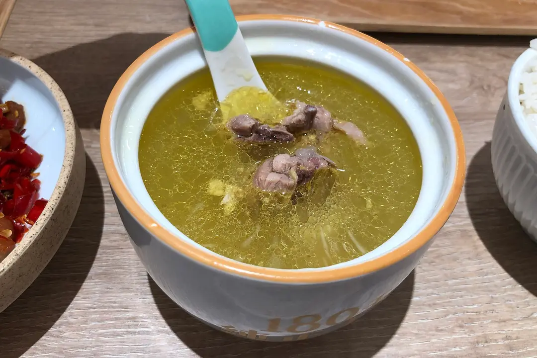 A bowl of clear golden Feixi old hen soup with pieces of chicken