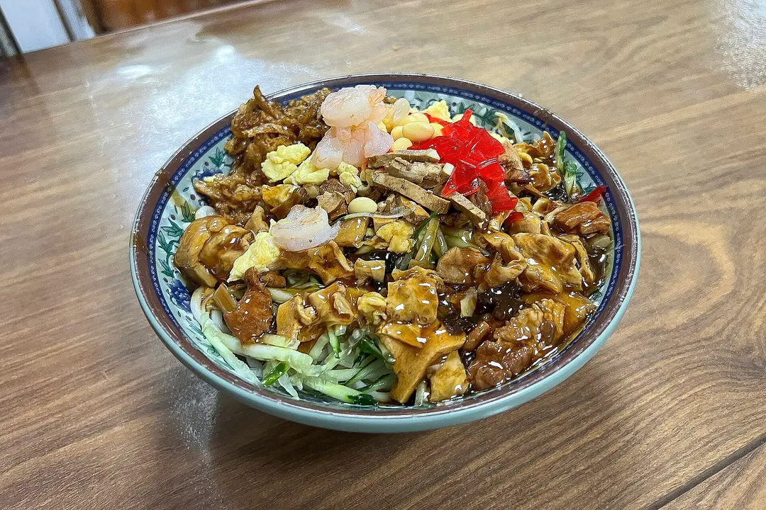 Bowl of noodles under brown gravy with shrimp, egg, red pepper and vegetables