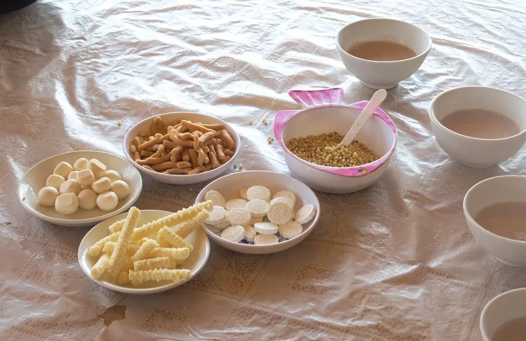 Plates of white dried-curd sweets and fried snacks, a bowl of roasted millet and bowls of milk tea