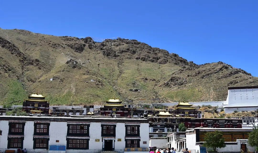 Gold-roofed halls and whitewashed buildings of Tashilhunpo Monastery below a bare brown mountain