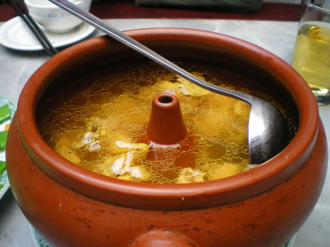 Golden chicken broth in a clay steam pot with a ladle