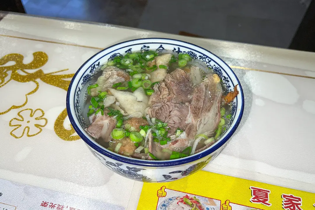 A blue-and-white bowl of clear lamb soup with sliced lamb, vermicelli and spring onion in Dunhuang