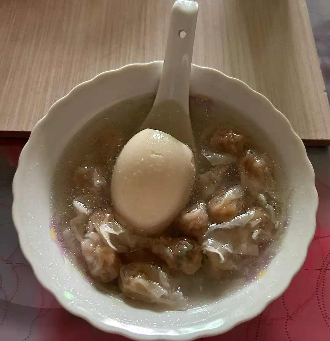 A bowl of rouyan wontons in clear soup with a whole duck egg on a spoon