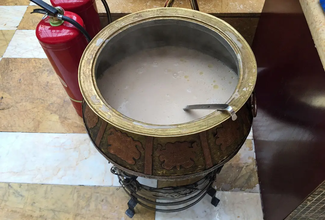 Pale milk tea steaming in a large brass-rimmed pot with a ladle, at a hotel in Hohhot