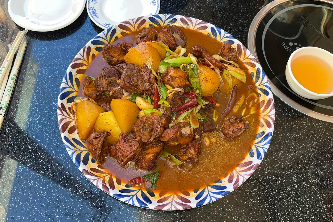 Big plate chicken with potato chunks, green chili and dried red chili in brown sauce, in Kashgar