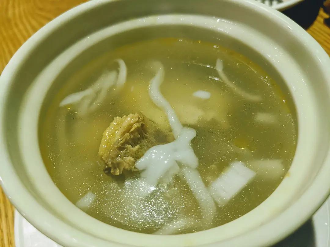 A bowl of coconut chicken soup with strips of coconut flesh in clear broth