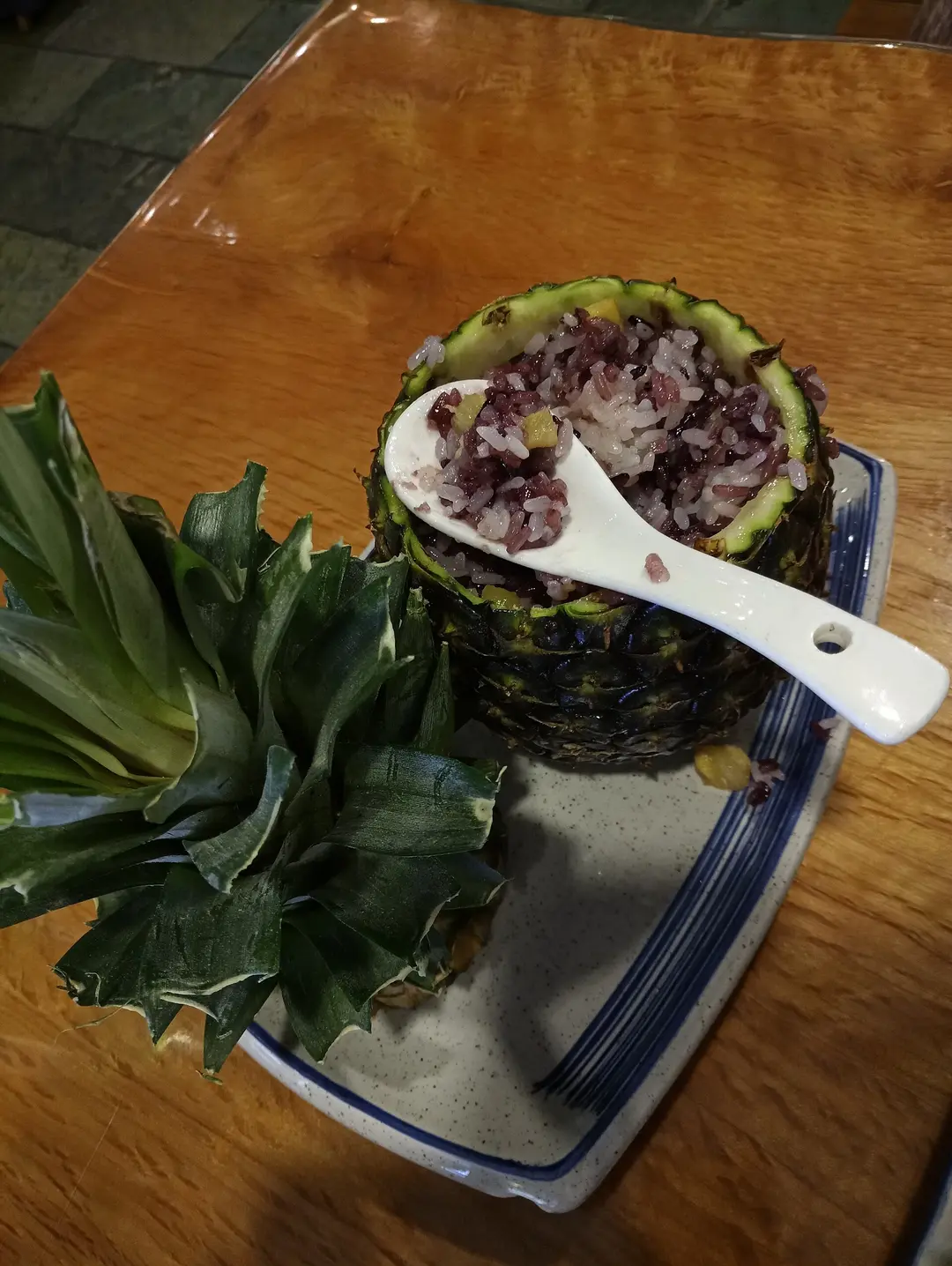 Purple and white sticky rice served in a hollowed pineapple with a spoon