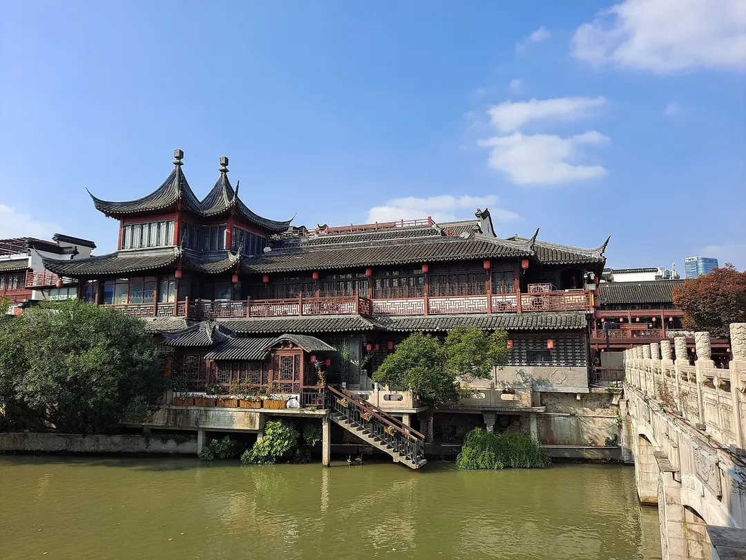 A two-story wooden building with upturned eaves beside a stone bridge on the Qinhuai River at Fuzimiao