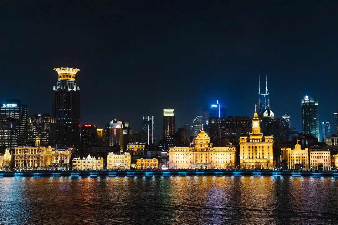 The lit stone buildings of the Bund reflected in the Huangpu River at night