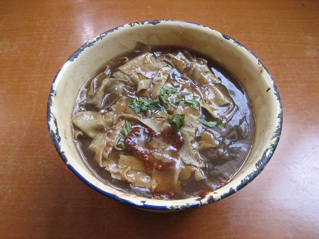Bowl of pancake strips in thick brown sauce topped with chili and coriander