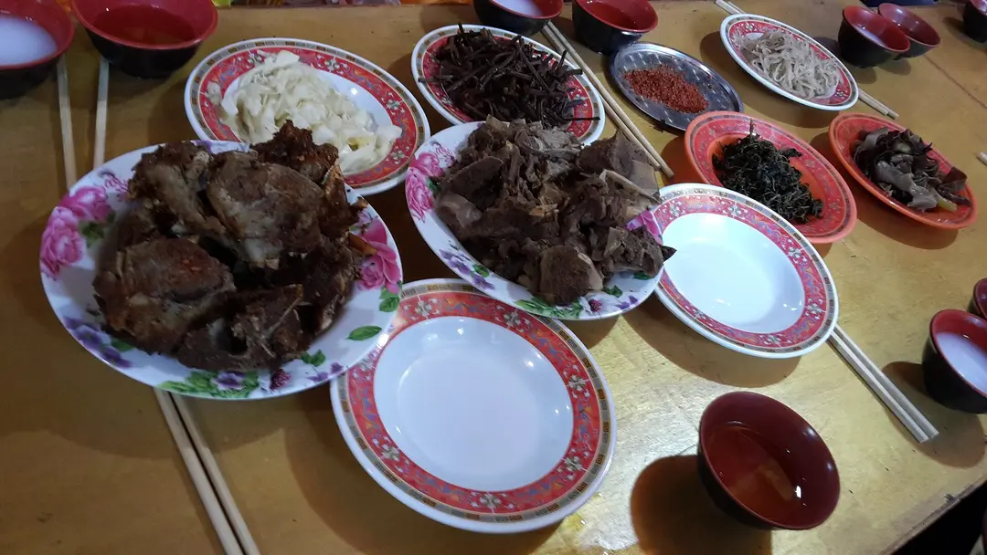 Plates of stewed yak and goat meat with pickles and barley noodles at a Tibetan meal in Jiuzhaigou County