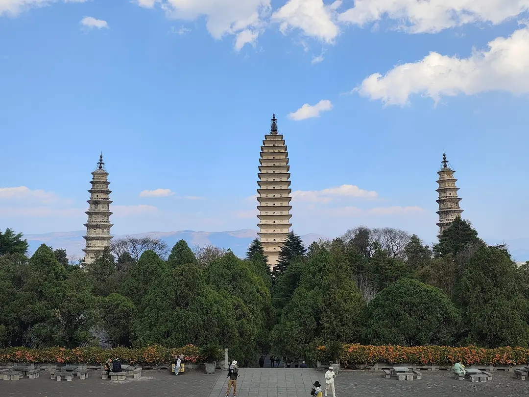 The three white pagodas of Chongsheng Temple rising above dark green trees under a blue sky