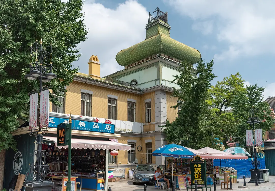 A yellow Russian-style building with a green onion-shaped roof and souvenir stalls on Russian Street