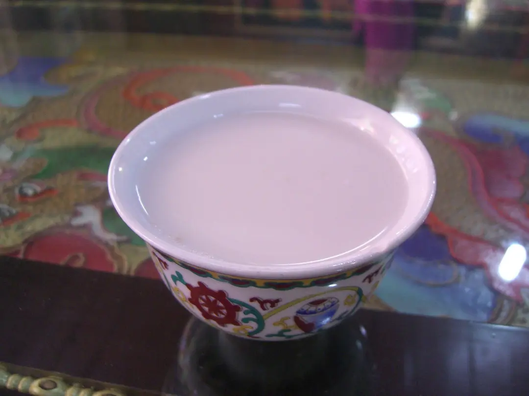 A painted porcelain cup filled with pale, milky butter tea on a glass-topped table