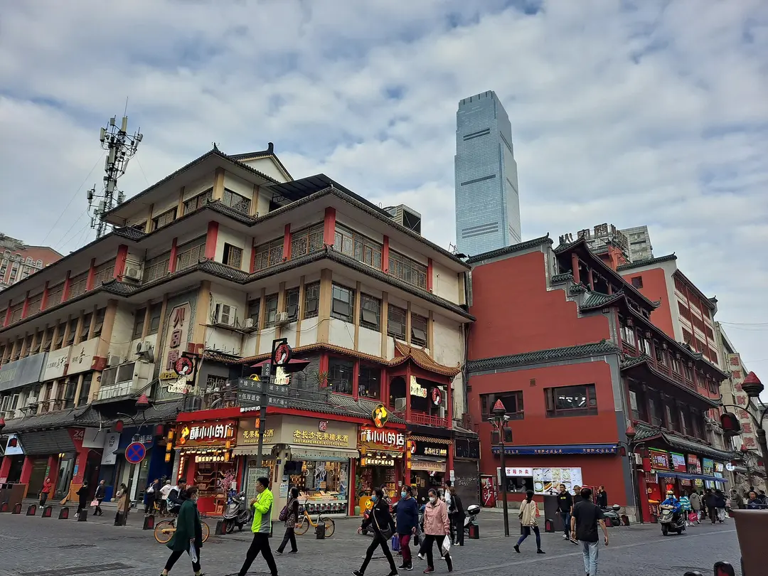 Old-style red and grey buildings full of snack shops on Pozi Street, with a skyscraper behind
