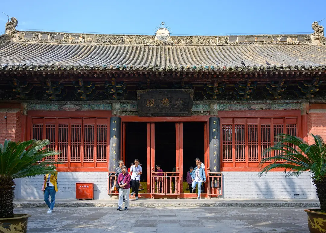 A red-walled hall with a tiled roof and a carved name board at White Horse Temple
