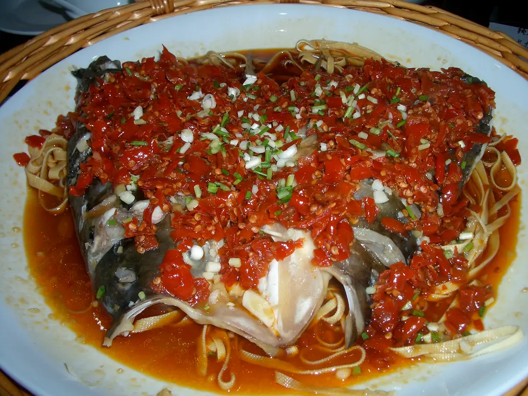 Steamed fish head covered in chopped red chilies and spring onion on a large plate