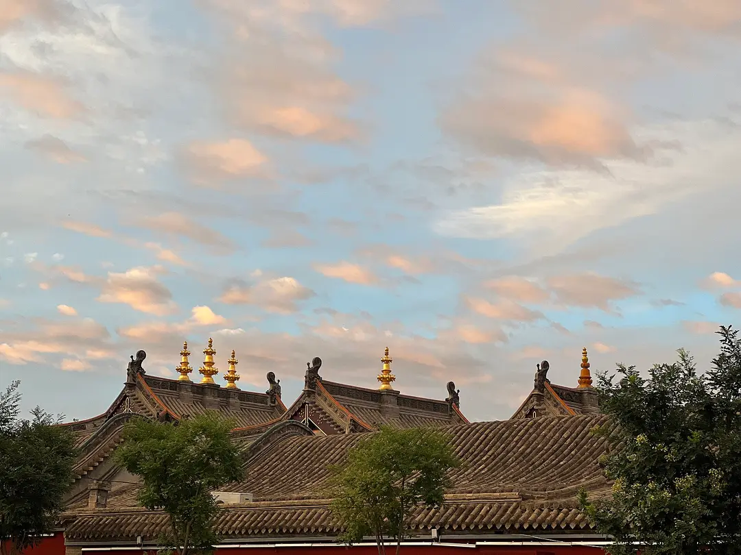 Grey tiled hall roofs of Dazhao Temple in Hohhot topped with gilded finials, under an evening sky