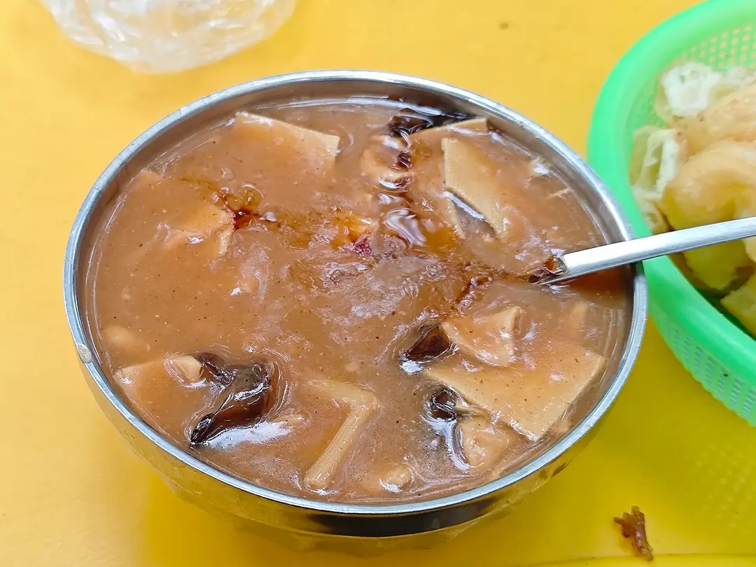 A metal bowl of thick, peppery hulatang with tofu skin and black fungus
