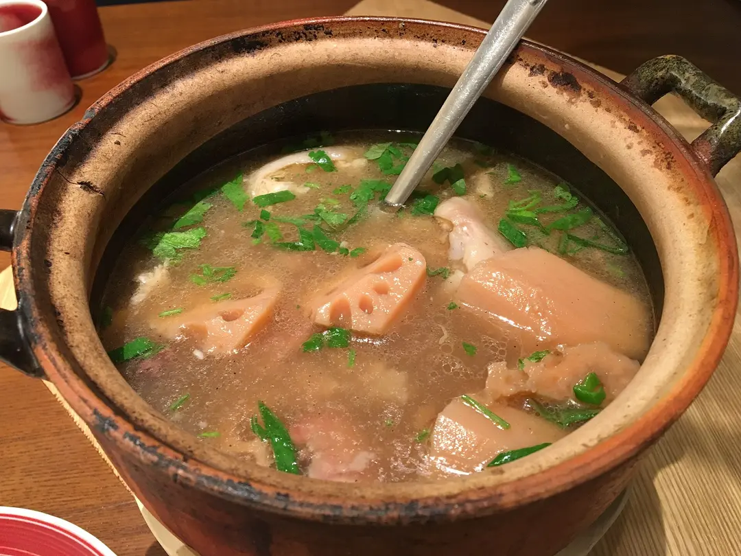 A clay pot of pork and lotus root soup with chopped scallions and a ladle
