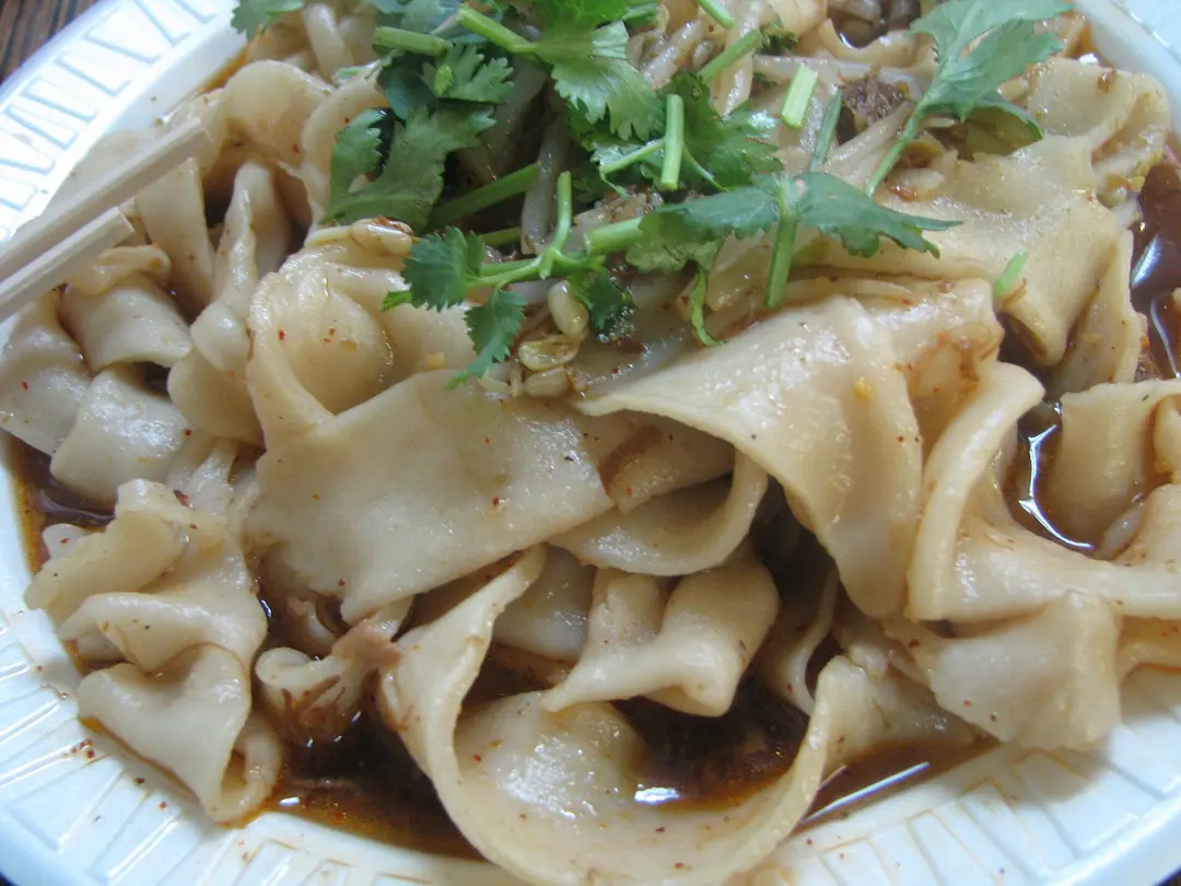 Wide, flat hand-pulled biangbiang noodles in a chili oil sauce, topped with fresh cilantro