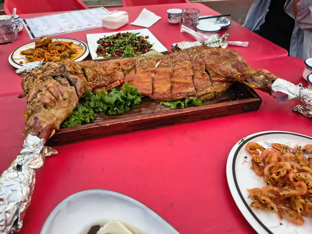 Half a roast lamb, golden and scored, sprinkled with sesame on a wooden board on a red table