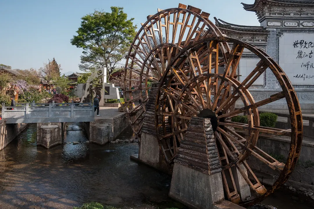 Large wooden water wheels beside a stream and footbridge at the entrance to Lijiang Old Town