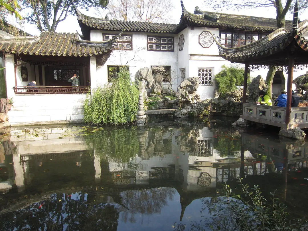 White-walled halls, latticed windows and rockery reflected in a pond in the Lingering Garden