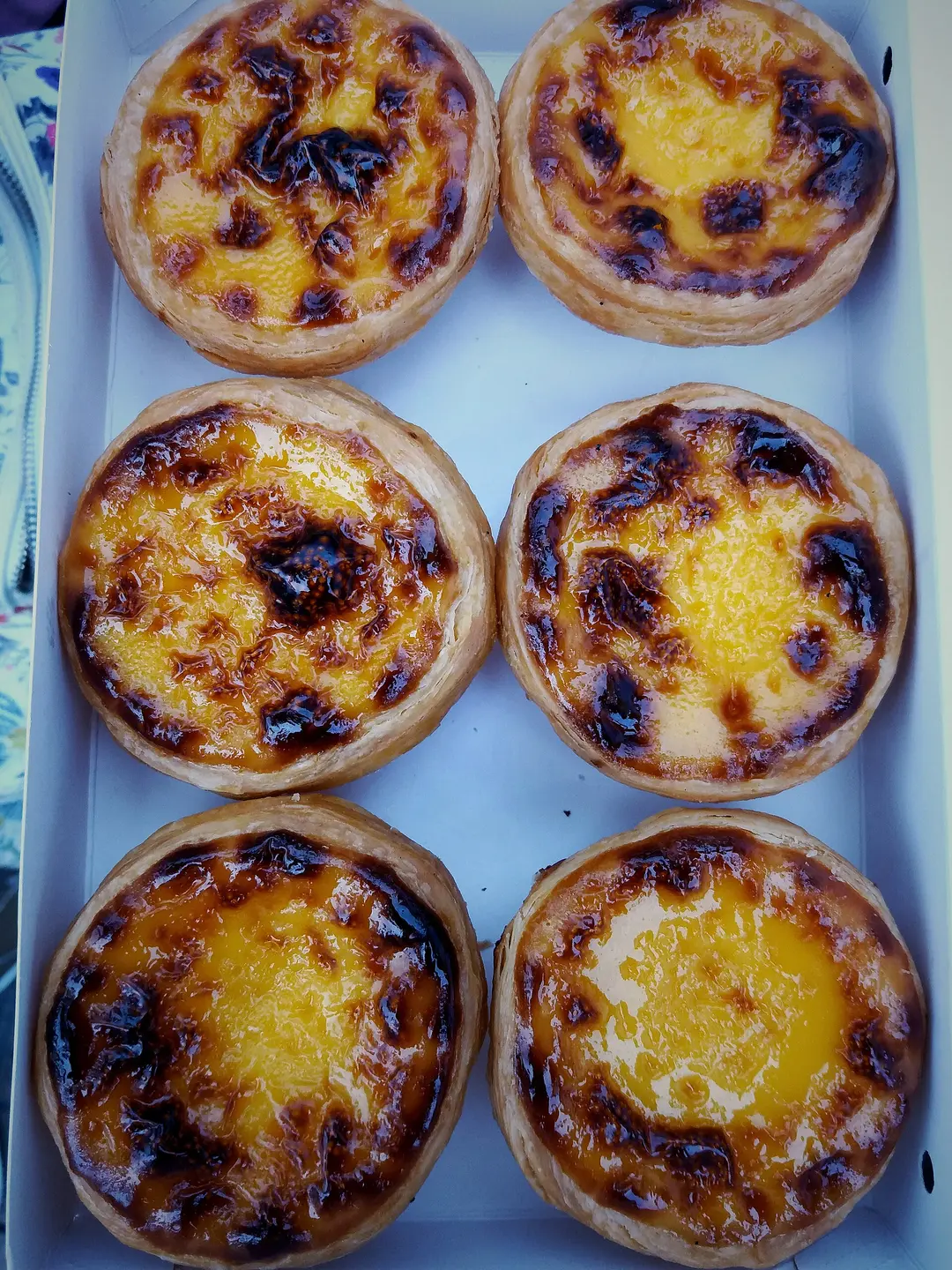 Six Portuguese egg tarts with caramelized tops in a white box