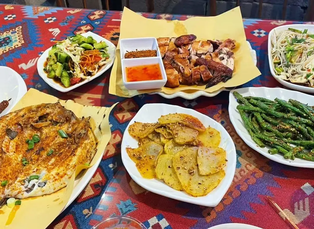 Plates of grilled fish, chicken, potato slices and green beans with chili sauce on a patterned cloth