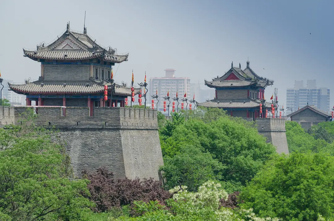 Two wooden gate towers on the Xi'an City Wall above green trees, with tall city buildings behind