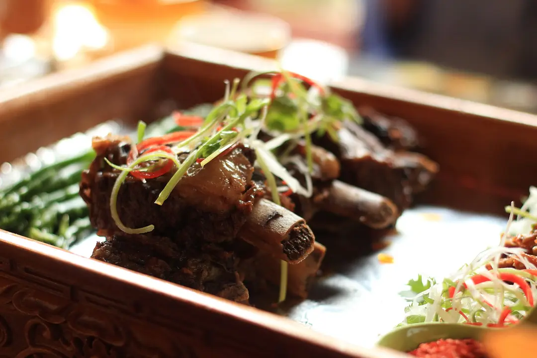 Braised yak ribs topped with sliced chili and spring onion in a carved wooden tray