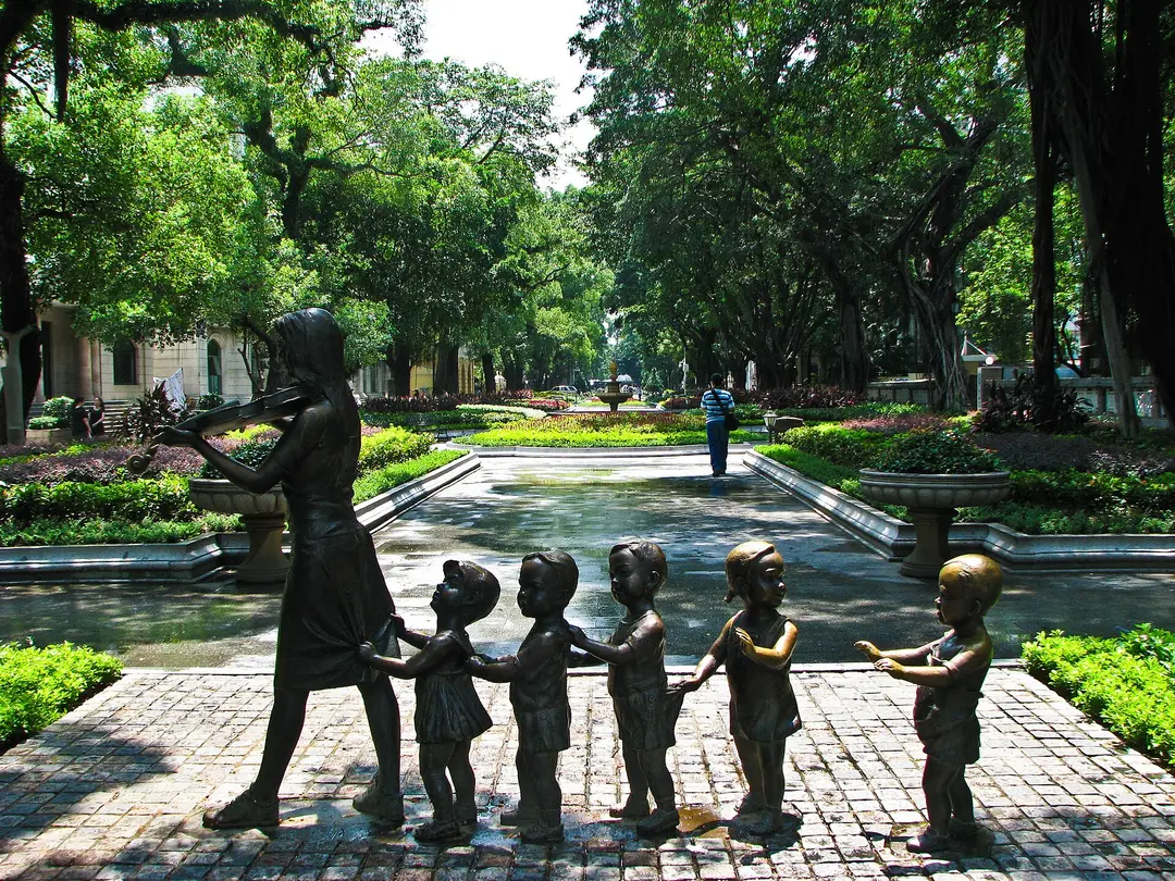 Bronze statues of a violinist and children on a garden path under banyan trees on Shamian Island