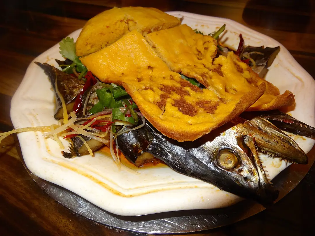 Whole salted fish on a plate under golden slices of corn cake, with shredded vegetables