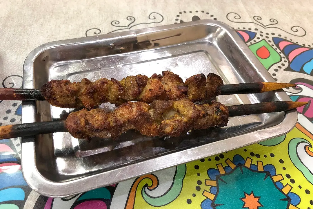 Two large grilled lamb kebabs on charred tamarisk-wood skewers in a metal tray