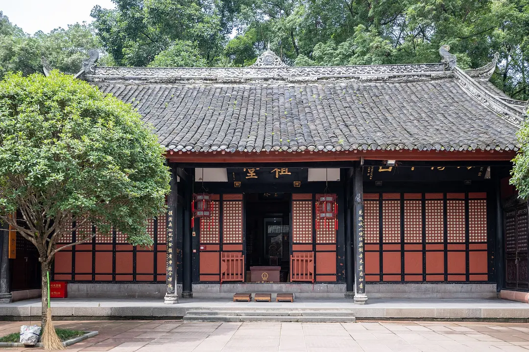 A temple hall with red wooden doors and a grey tiled roof in a courtyard at Wenshu Monastery