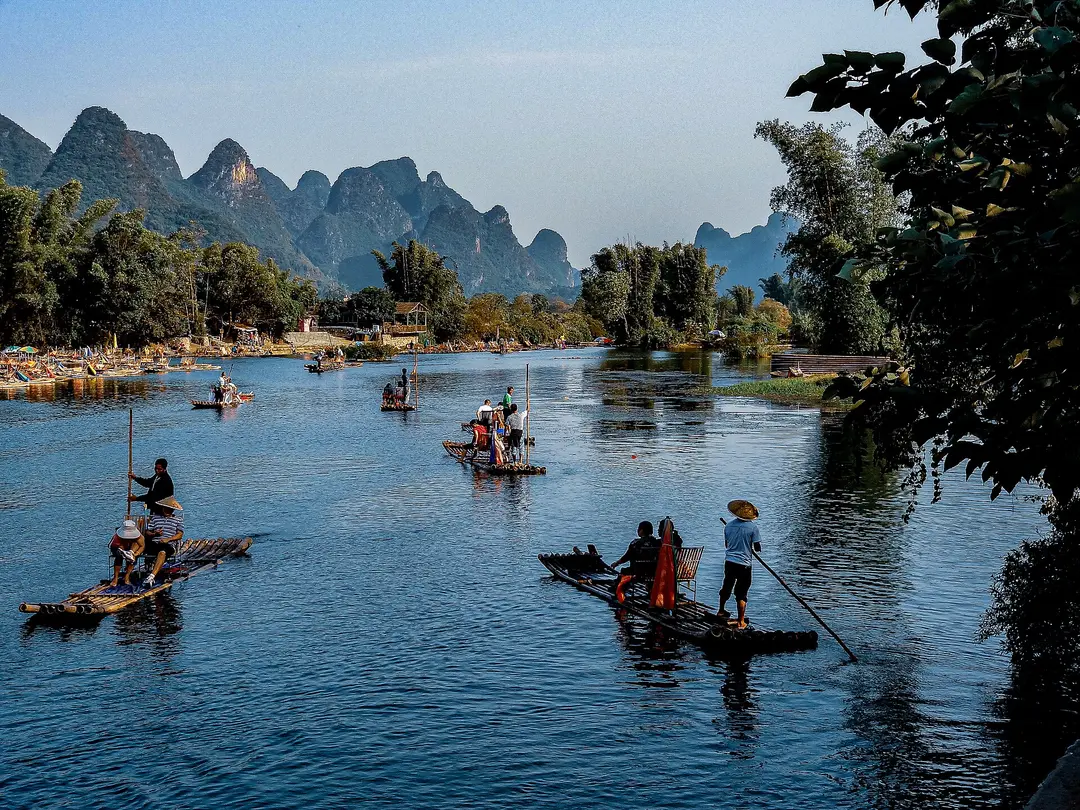 Bamboo rafts poled by boatmen in straw hats on the Yulong River, with karst peaks behind