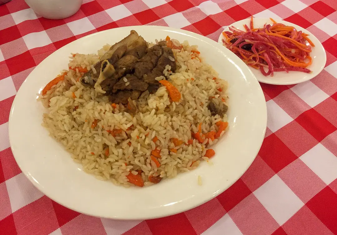 A plate of polo, rice with carrot and lamb on the bone, beside a small plate of shredded vegetable salad